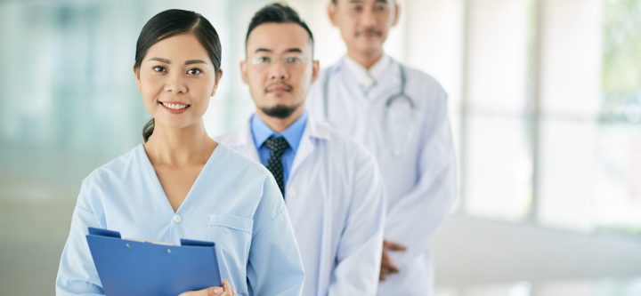 Portrait of pretty Vietnamese female doctor and her coworkers behind