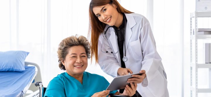 Asian medical doctor take care and explain senior elderly woman female patient on wheelchair with tablet, looking at camera